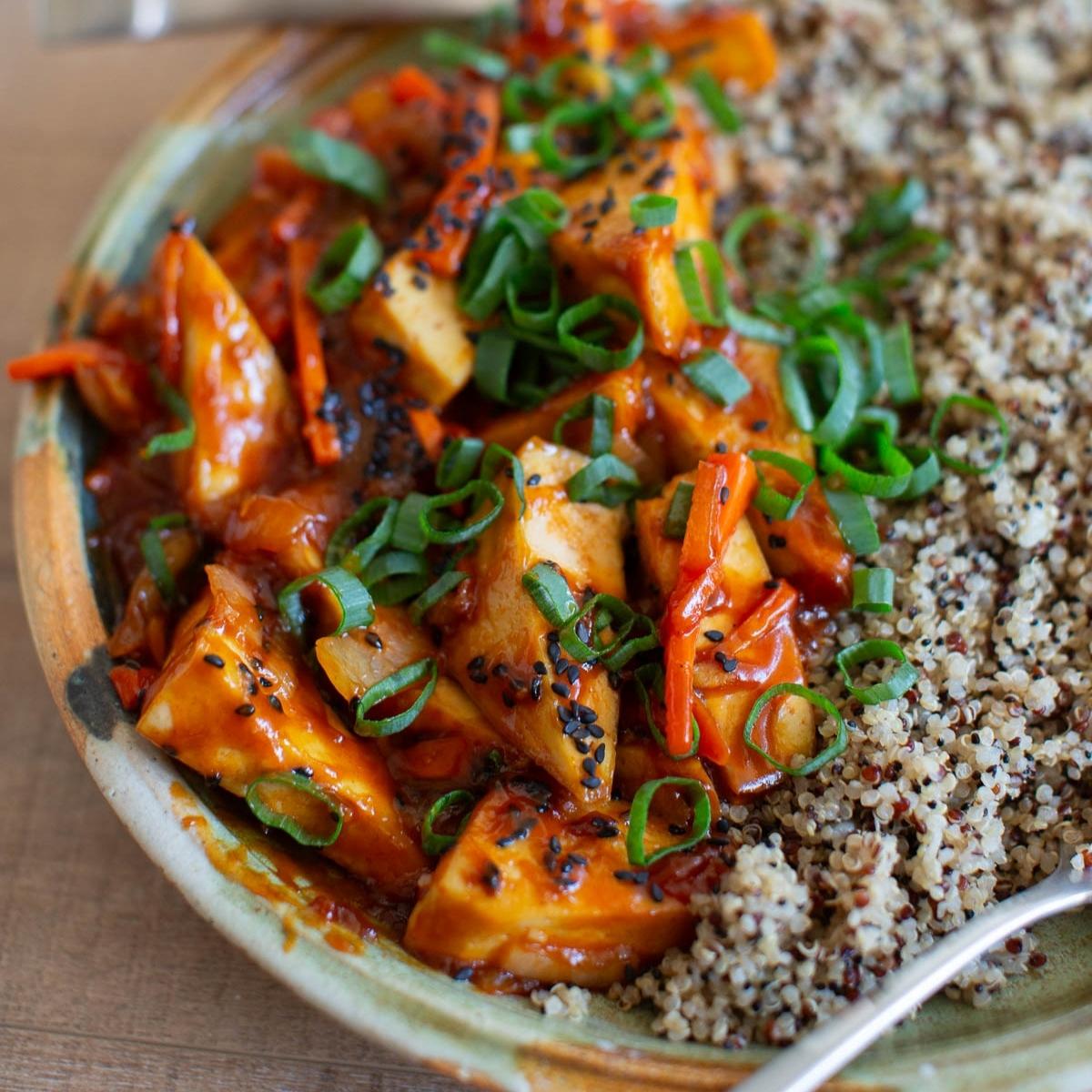 A bowl of sweet and sour tofu topped with sliced green onions and served with quinoa.