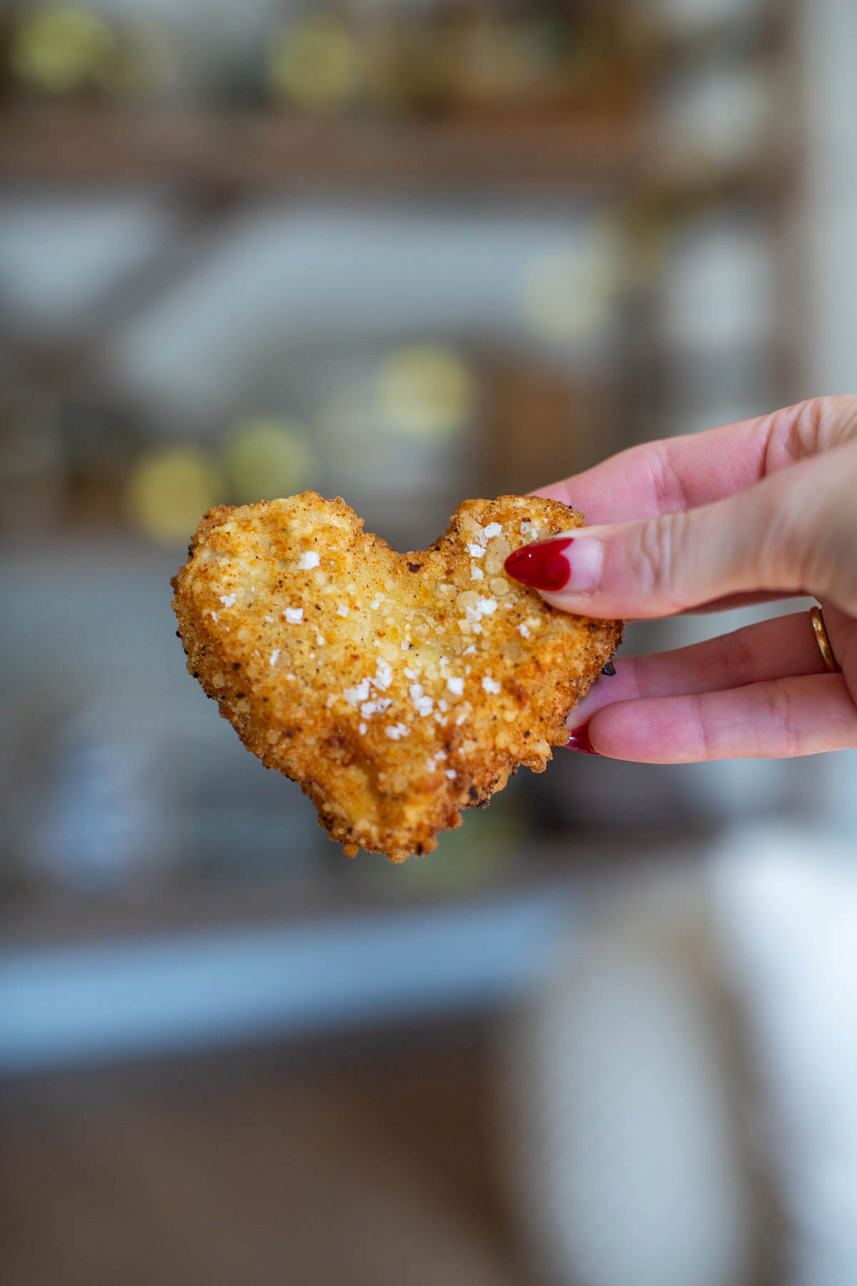 A hand with valentine fingernail holding a deep fried tofu heart for a vegan fried chicken recipe.