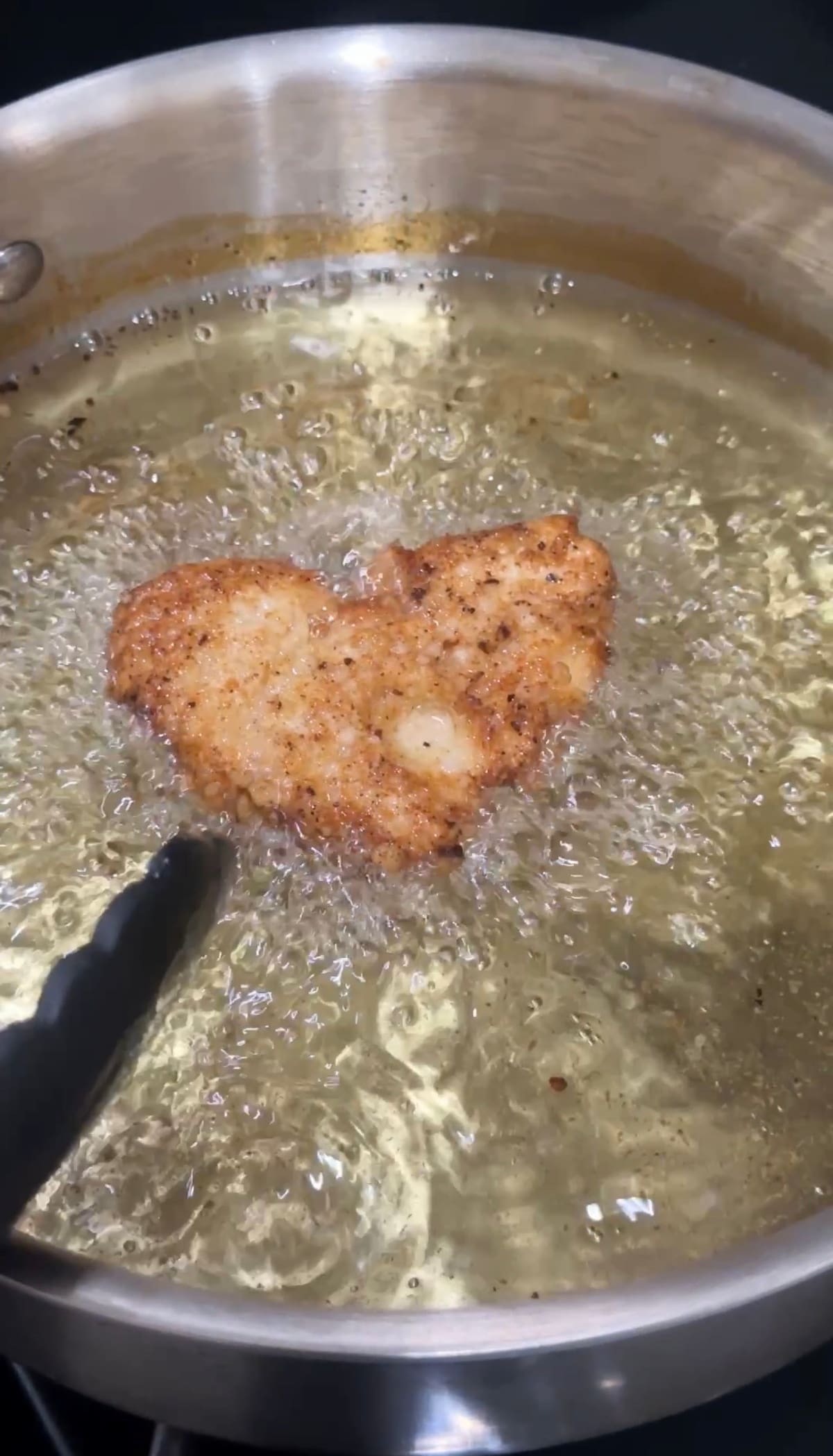 A piece of heart-shaped vegan fried chicken (deep fried tofu) sizzling in oil.
