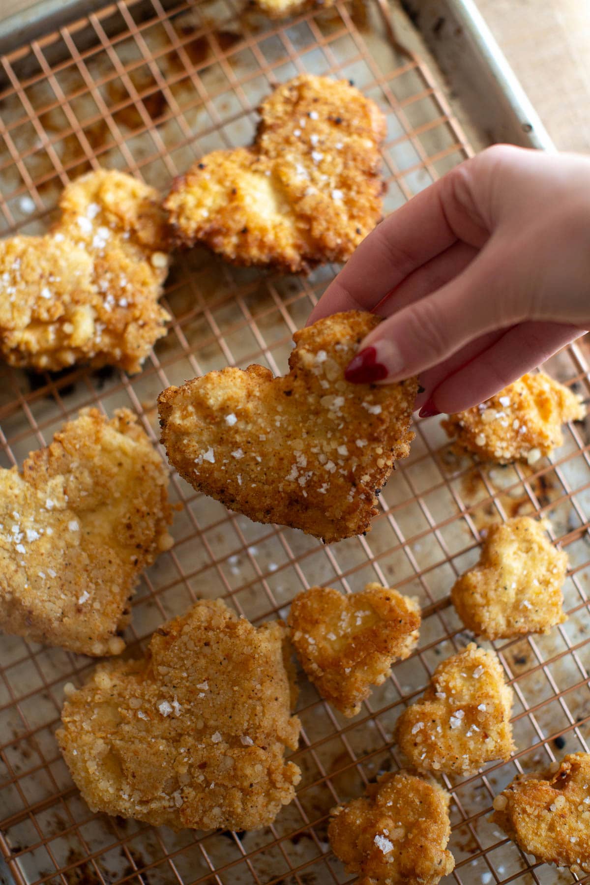 Fingers holding one of the deep fried tofu hearts above a tray of cooling vegan fried chicken.