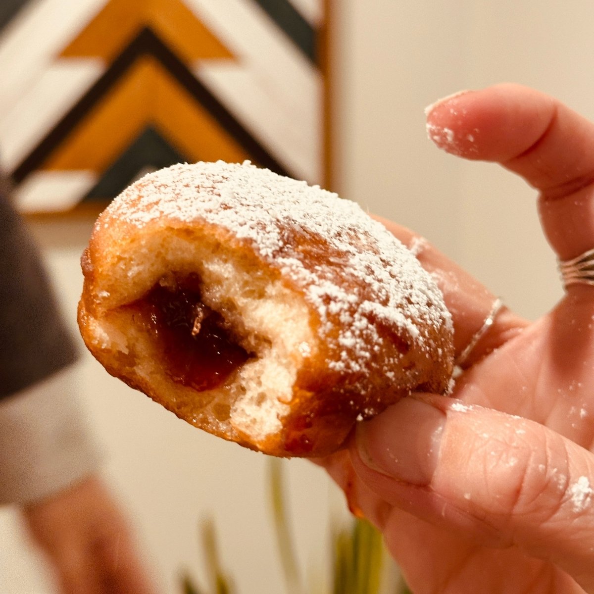 A hand holding a vegan sufganiyot jelly jonut against a black, brown and white graphic background.