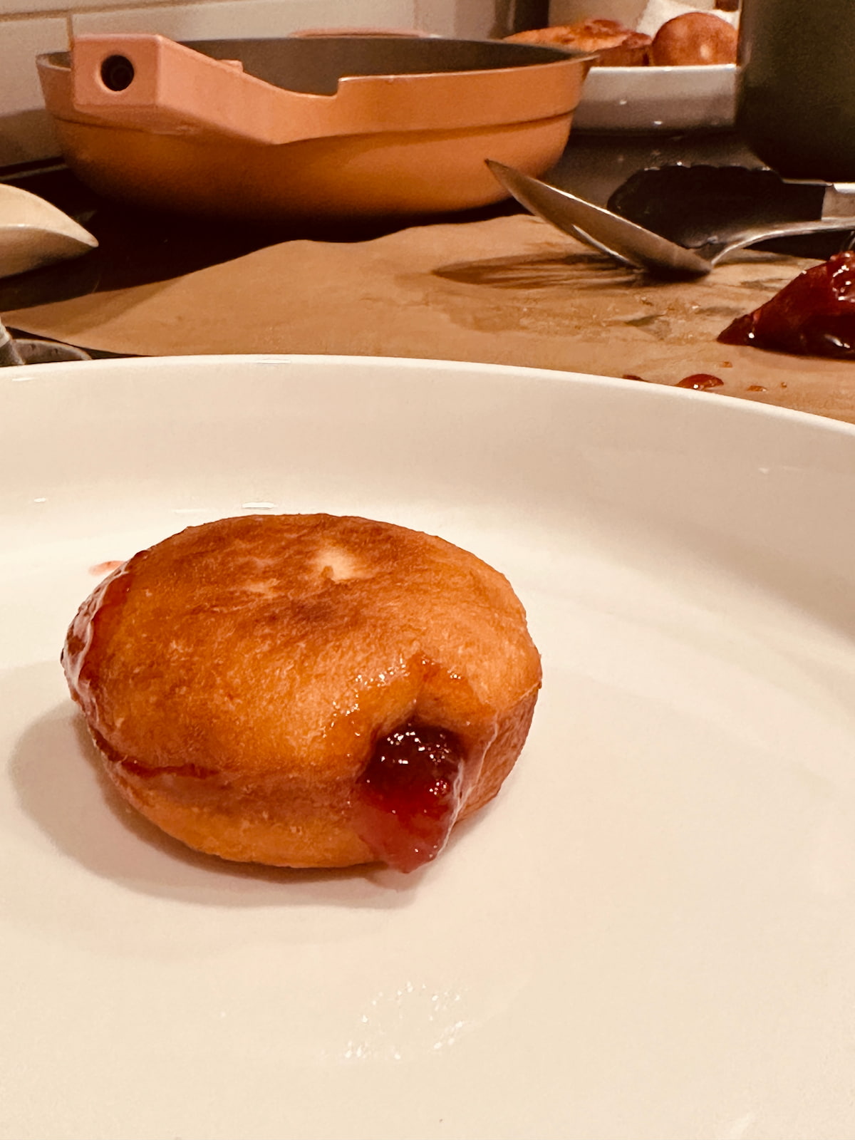 An un-powdered vegan sufganiyot on a white plate with jelly oozing out of the center.