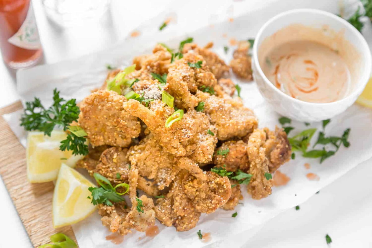 Oyster mushroom fried chicken, lemon wedges and a white bowl of sauce on white parchment paper.