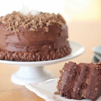 German raw vegan chocolate cake on a cake platter and next to a slice of cake on a white plate.