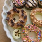 Fresh apple donuts with various toppings in a white serving dish.