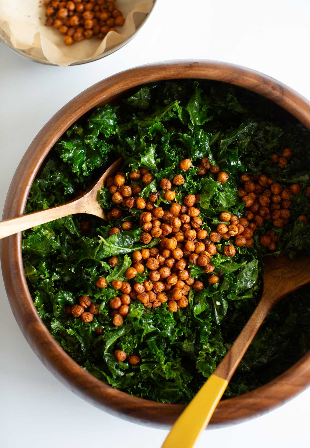 A beautiful wooden bowl of massaged kale salad topped with roasted chickpeas.