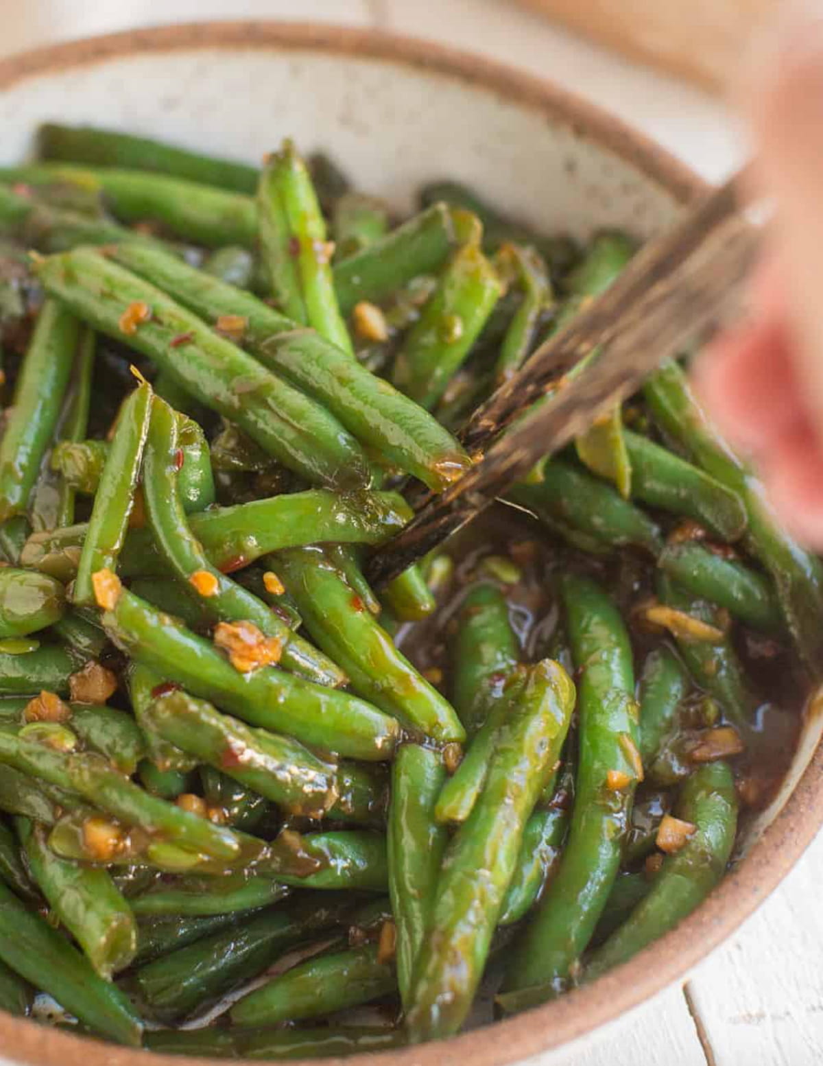 Close up of a pair of chopsticks grabbing a portion of sizzling Chinese green beans from a bowl.