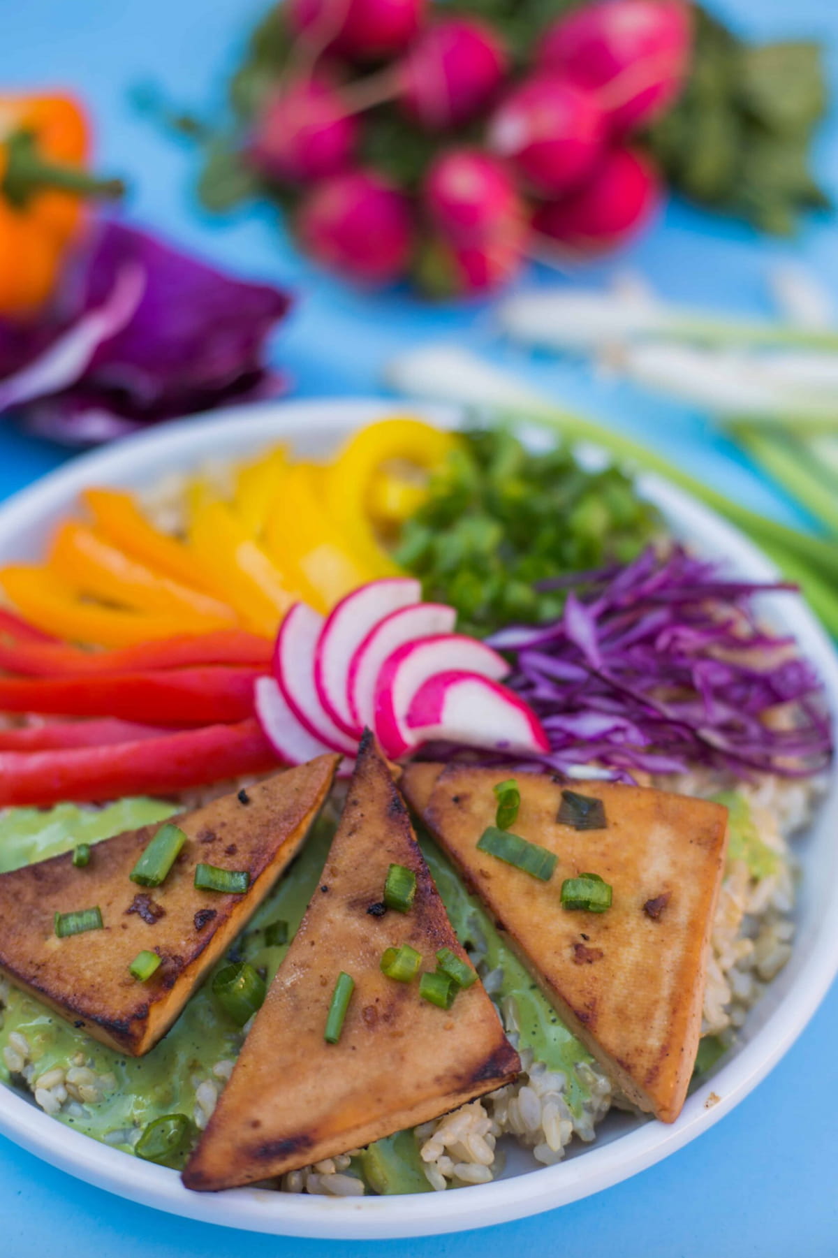 A buddha bowl with cilantro tahini dressing next to a bunch of fresh green onions and radishes.