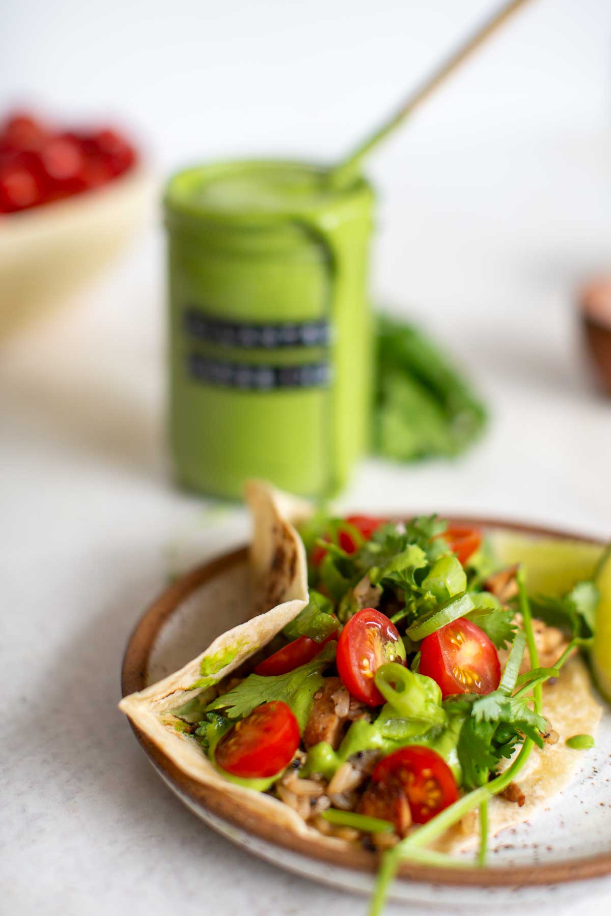 Homemade cilantro tahini dressing drizzled on a vegetable taco with a jar of dressing in the background.