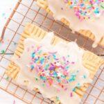 Two vegan pop tarts with frosting and vegan sprinkles on a copper baking rack.