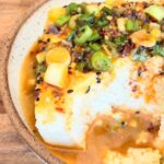 A bowl with chili oil tofu recipe and a scoop taken out of it.