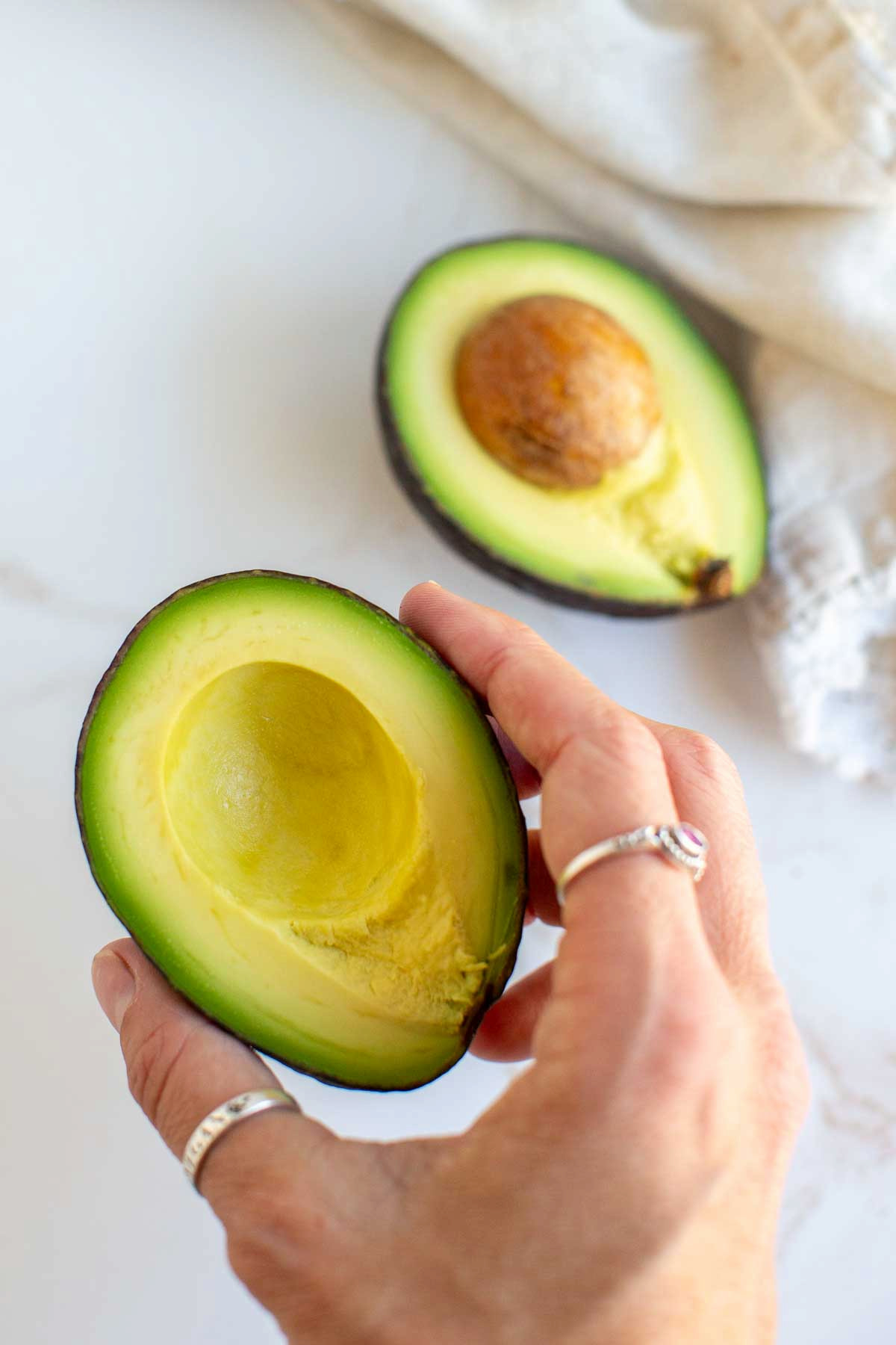 A hand holding a half of a fresh avocado for a vegan ranch dressing with avocado.