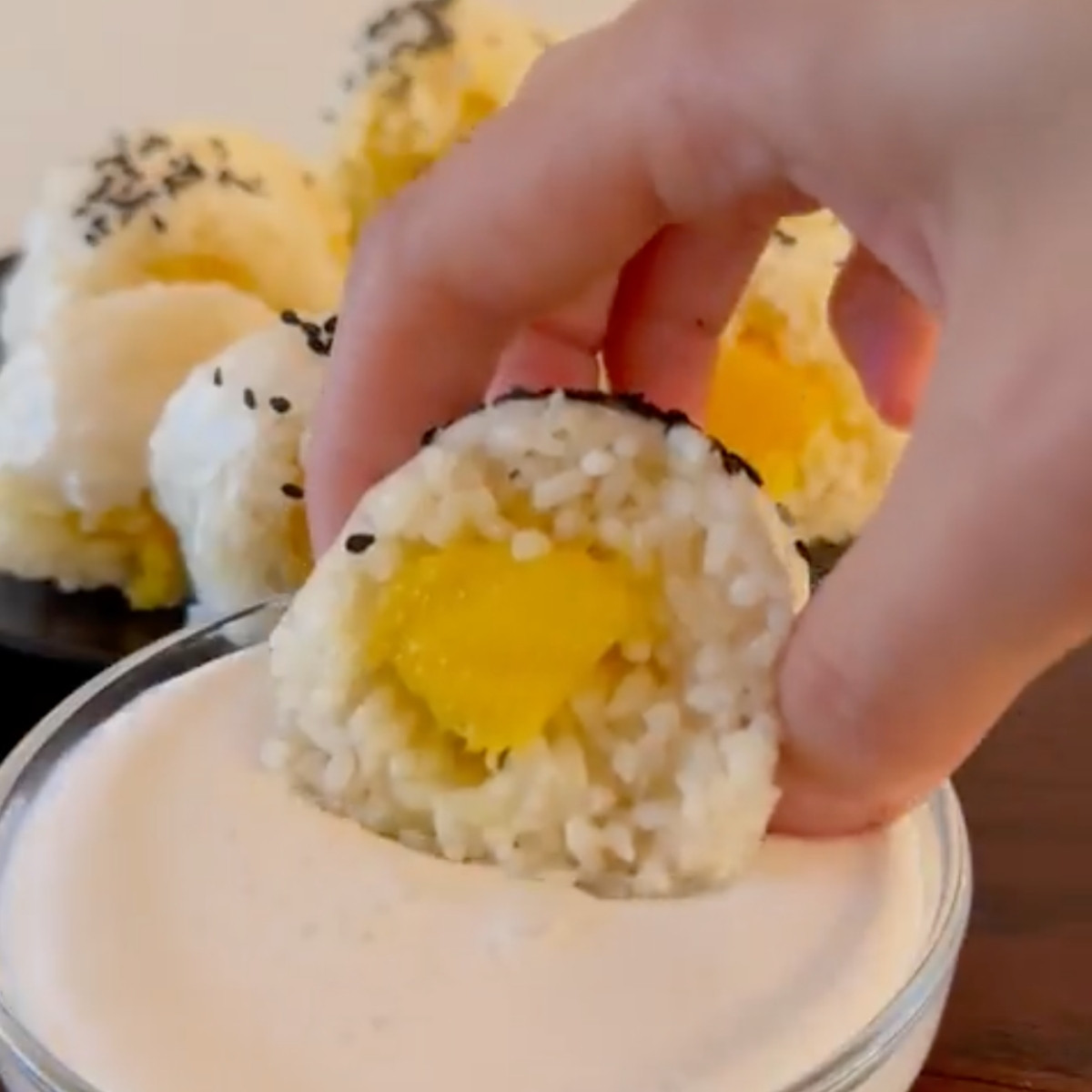 A slice of mango sticky rice spring roll being dipped into a sweet coconut sauce.