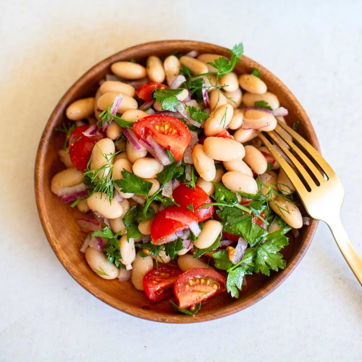 White bean salad recipe in a small wooden circular plate next to a gold fork.