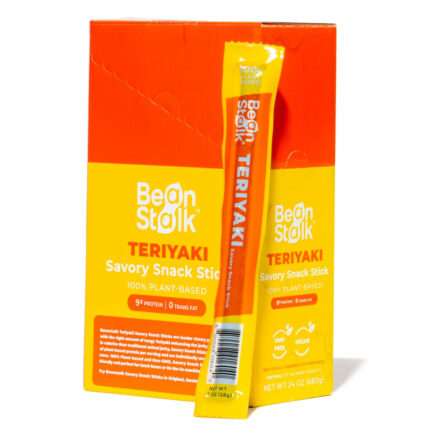 An orange and yellow box of Bean Stalk vegan jerky with an individual stick standing up in front of the box.