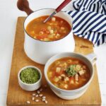 A wooden cutting board with a large bowl and small cup of vegan French pistou soup.