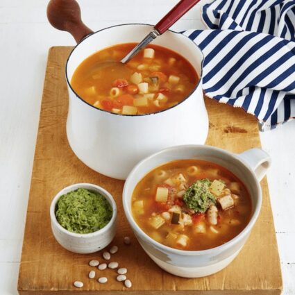 A wooden cutting board with a large bowl and small cup of vegan French pistou soup.