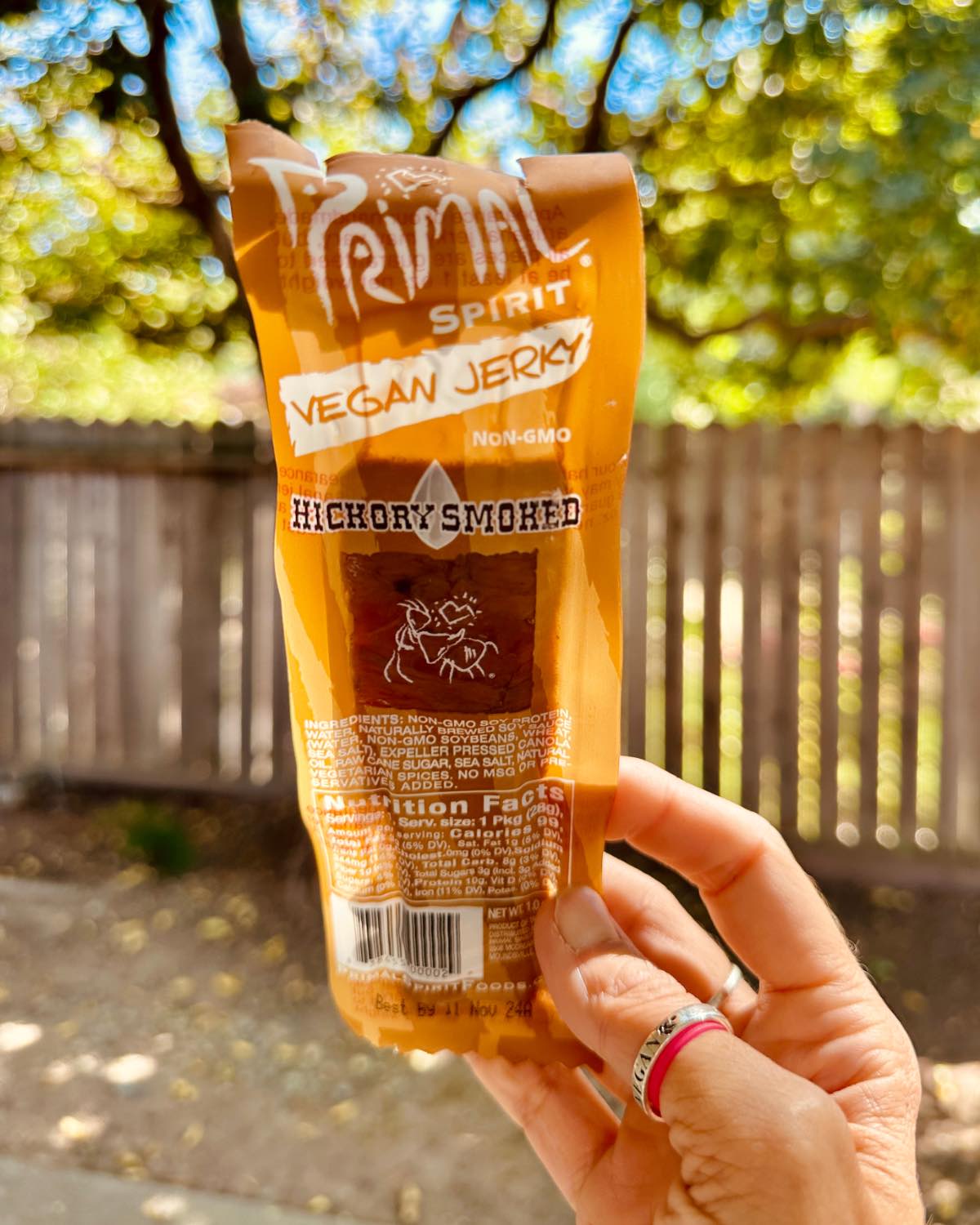 Holding out a strip of primal spirit foods jerky in the package outdoors.