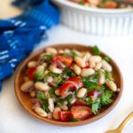 Delicious fresh white bean salad with tomatoes, herbs, and dressing served on a small wooden