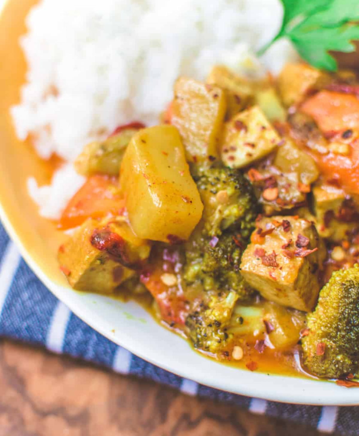A white plate of yellow curry with tofu, veggies, and white rice.