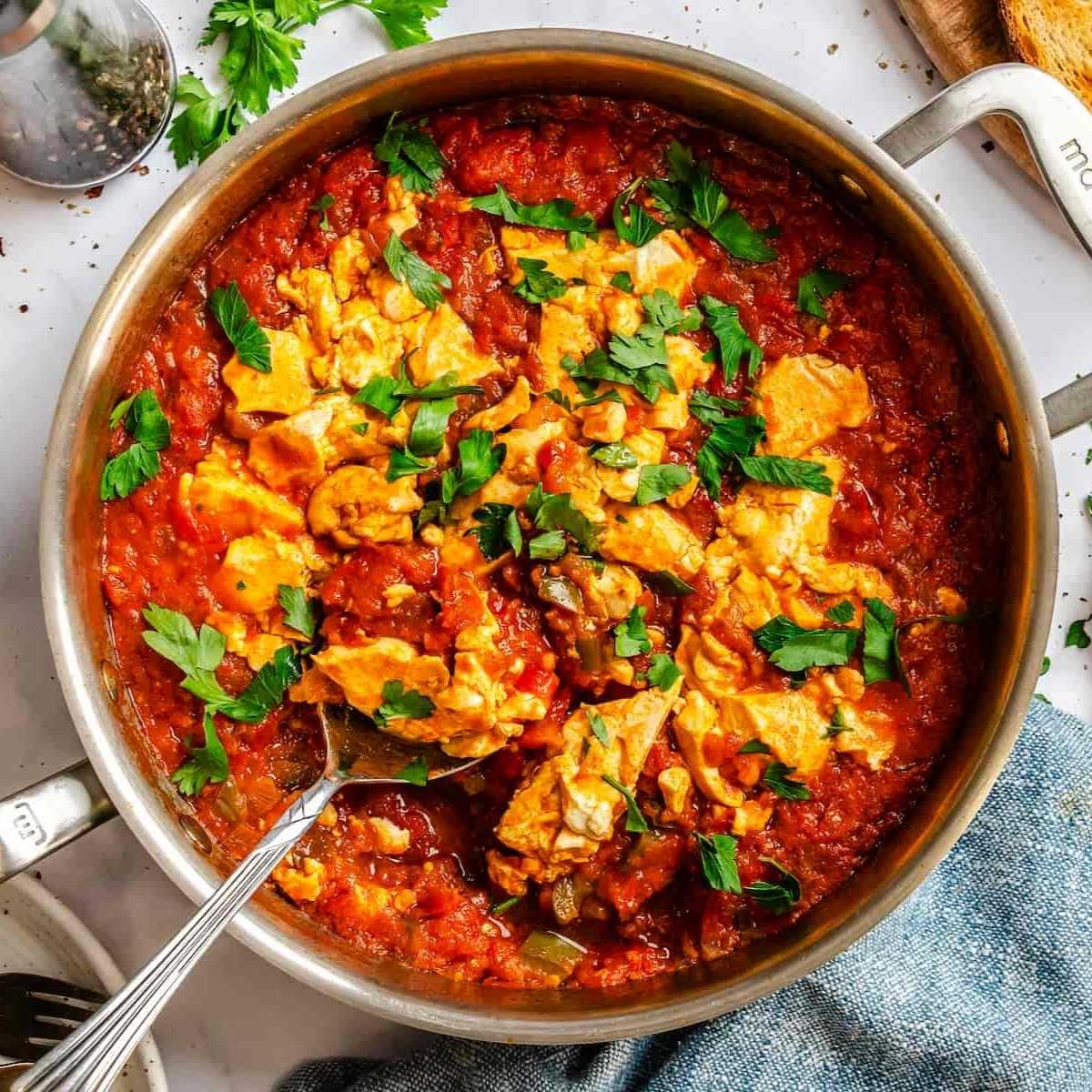 Vegan shakshuka recipe in a skillet with a silver serving spoon and garnished with fresh parsley.