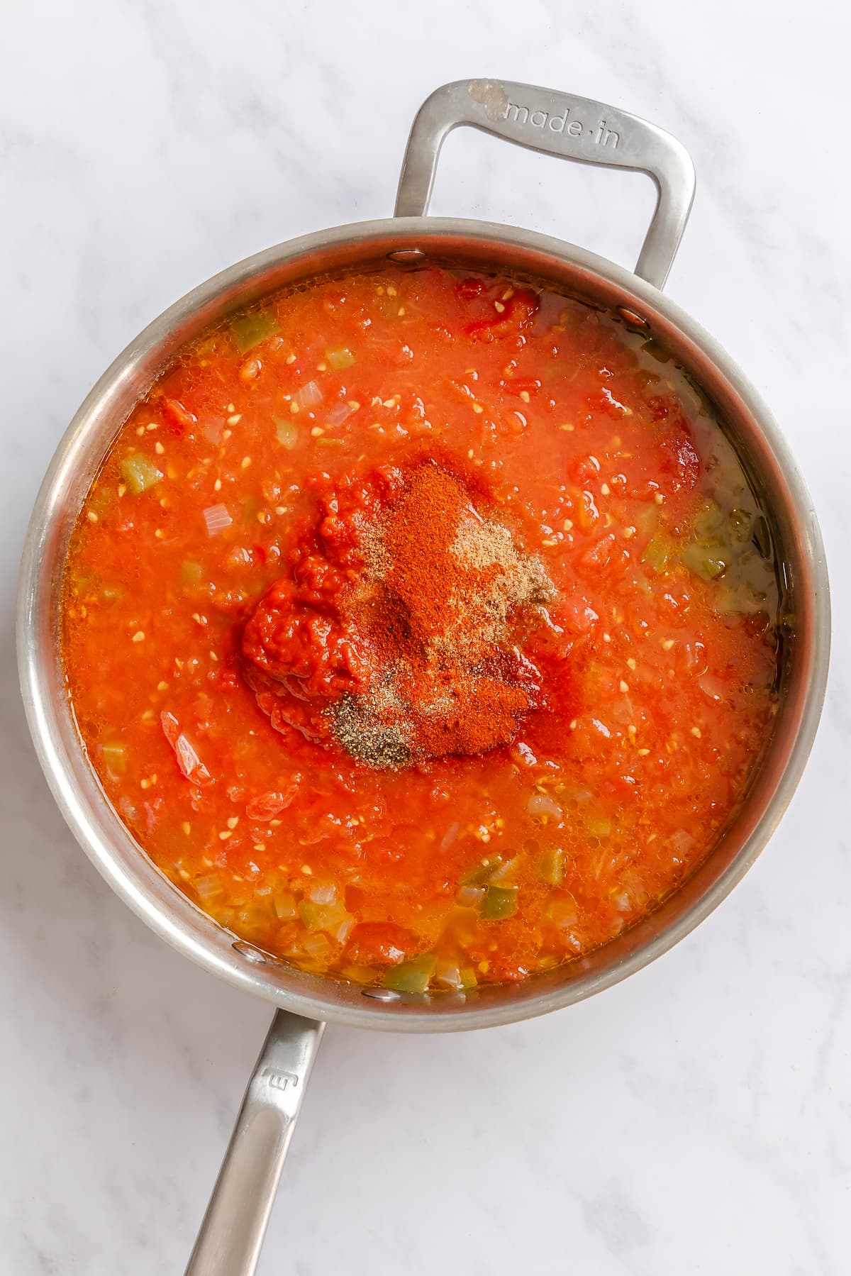Spices and tomato sauce added to crushed tomato mixture for a vegan shakshuka recipe.