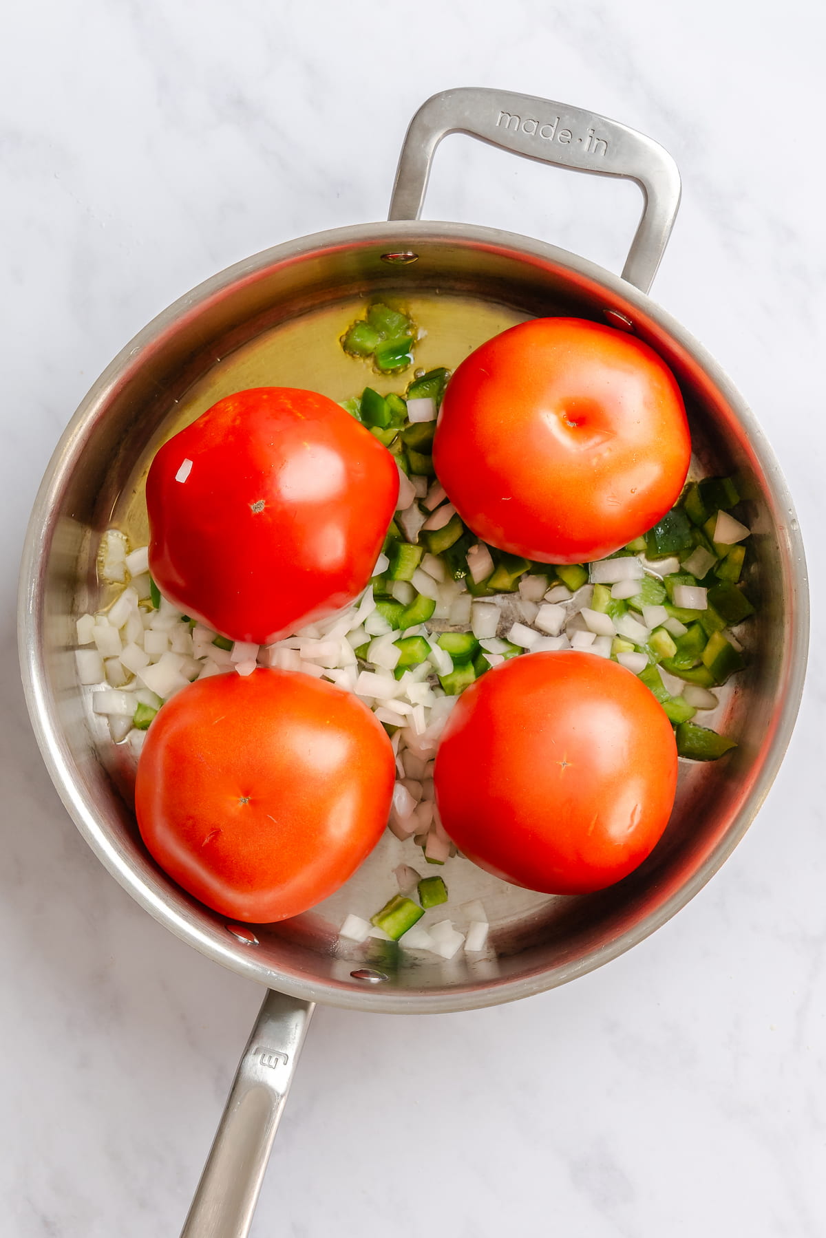 Whole tomatoes in a skillet with sauteed onions and bell peppers in olive oil for a vegan silken tofu shakshuka.