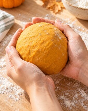A woman holding pumpkin noodle dough rolled into a big ball.