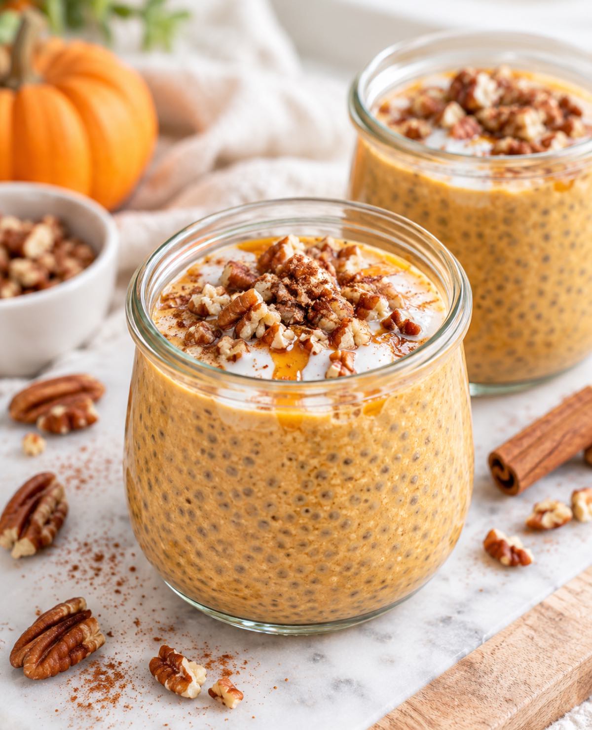 Glass jars of pumpkin pie chia pudding with fall toppings.