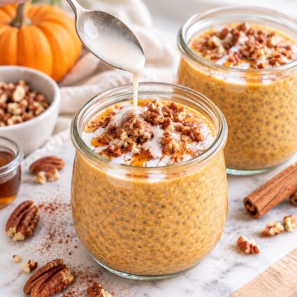 Glass ramekins with pumpkin pie chia pudding topped with chopped pecans, coconut cream, and pumpkin pie spice.