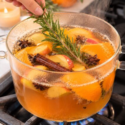 A glass pot with simmering festive fall smelling orange peels, cinnamon, rosemary, and pumpkin pie spice.